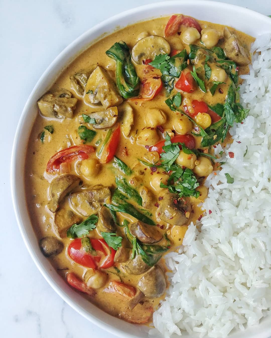 a vegan curry meal with white rice in aa white bowl sitting on a white marble countertop